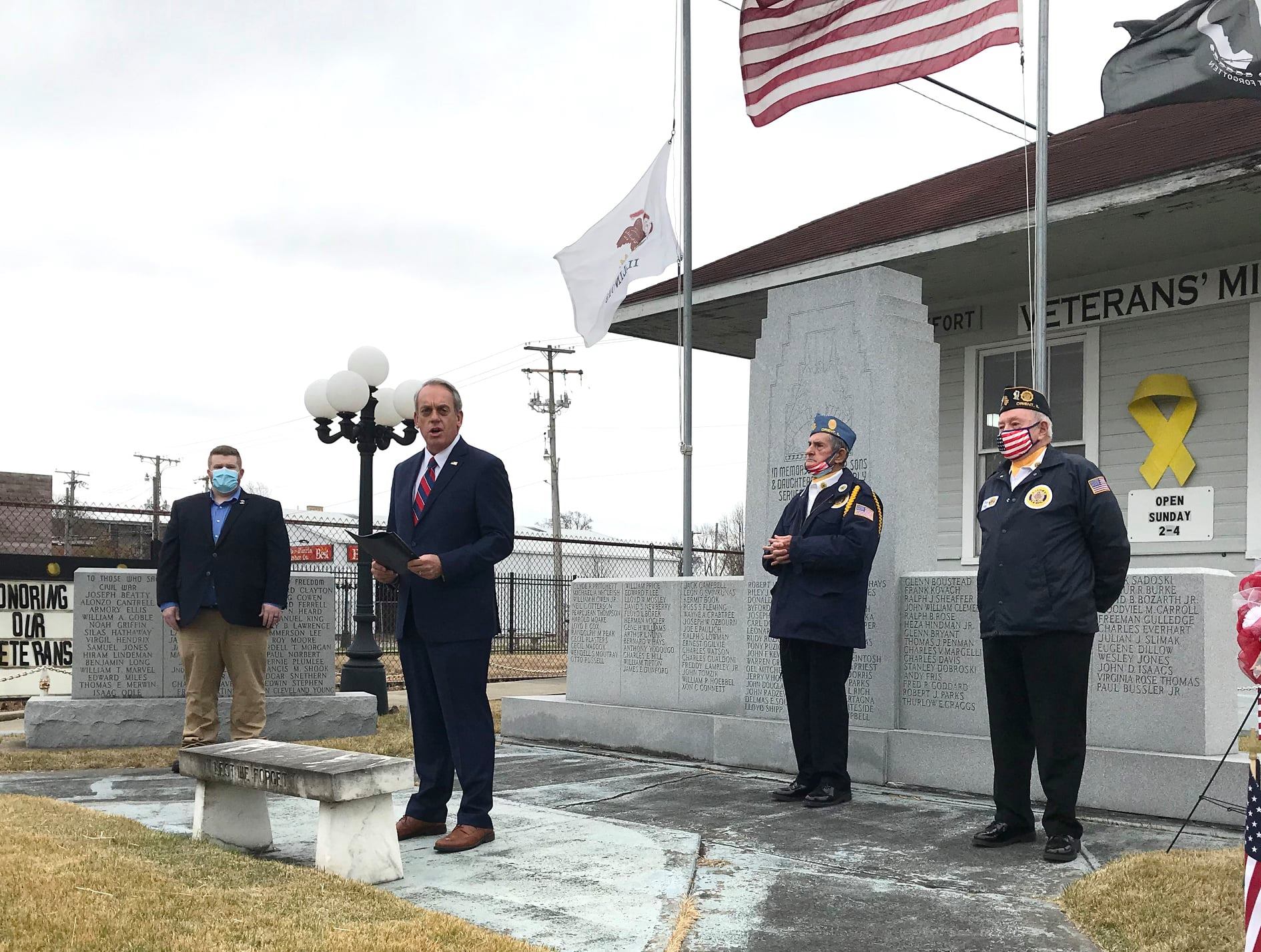 Outdoor commemorative event at the monument with speakers and honor guard