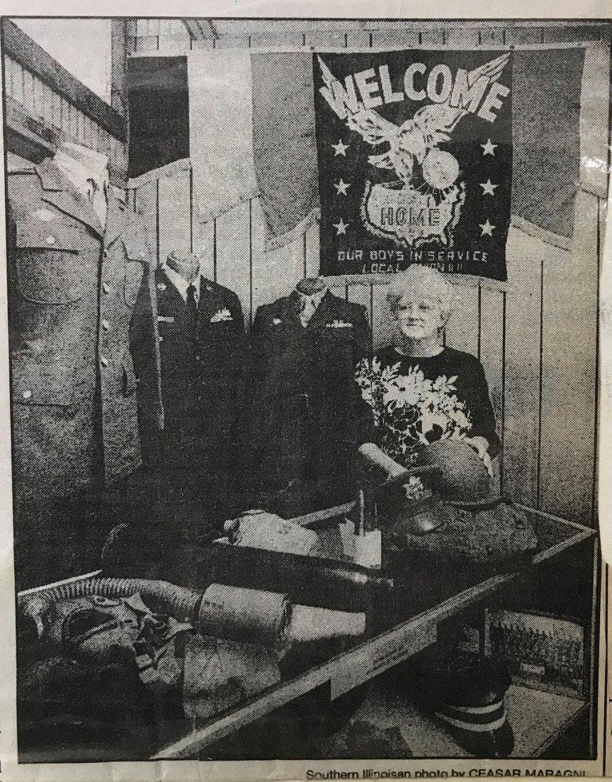 Historical newspaper clipping of a woman standing in front of military displays